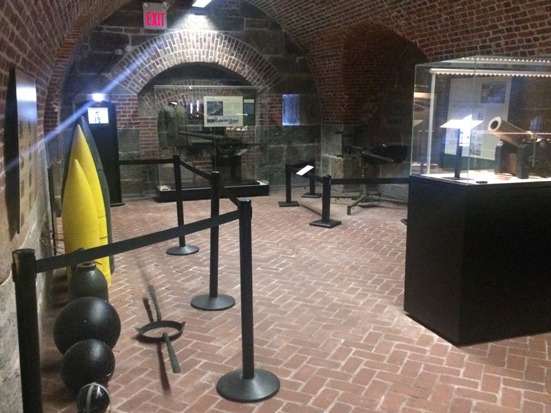 A room inside the Harbor Defense Museum with brick flooring and walls with several exhibits on display.